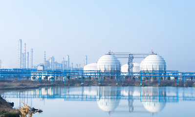 Marine-side storage vessels and industrial infrastructure reflected across calm water